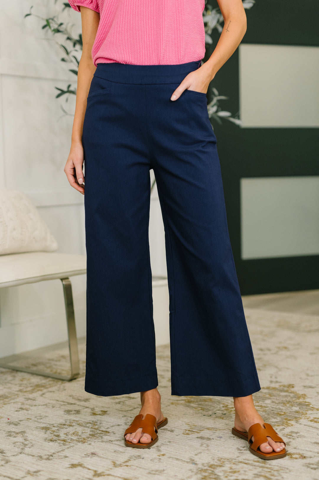 Close-up of navy wide-leg cropped pants with elastic waistband and side pockets, styled with tan slide sandals.
