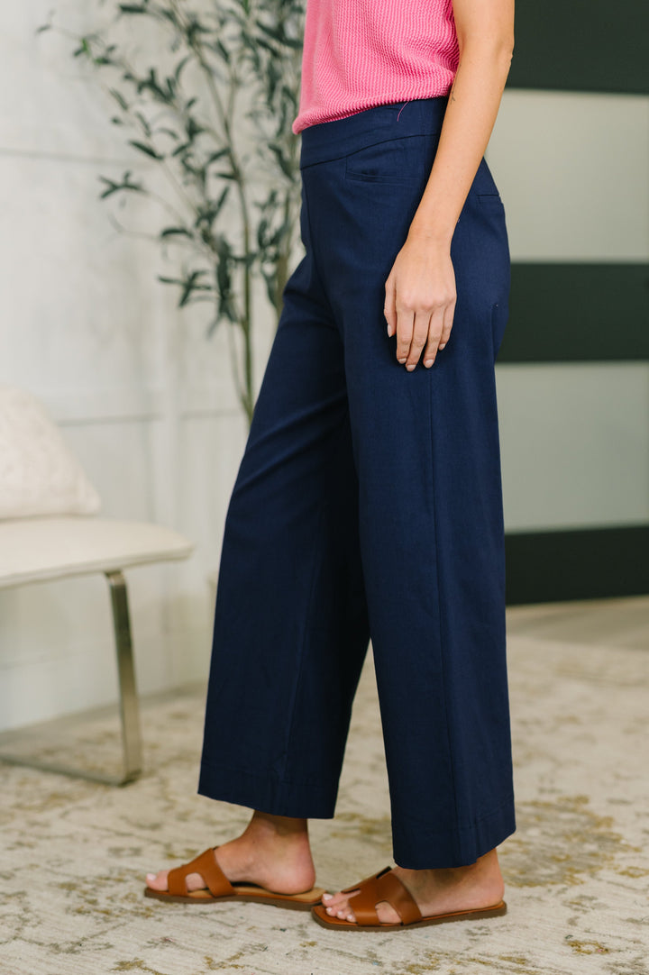 Side view of navy wide-leg cropped pants showing clean wide-leg silhouette and cropped length, styled with tan slide sandals.