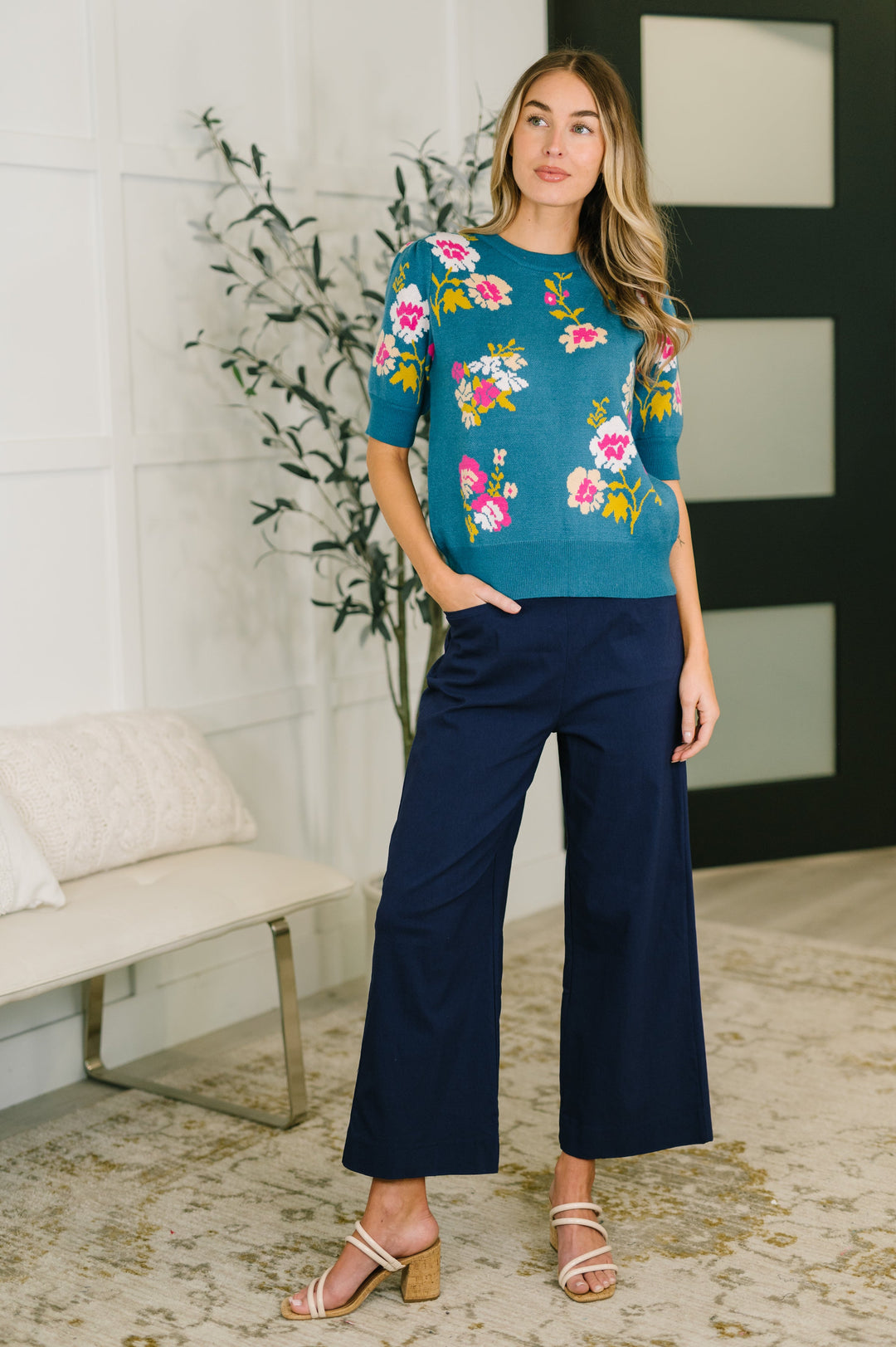 Woman wearing navy wide-leg cropped pants with elastic waistband, styled with a teal floral sweater top and strappy heeled sandals.