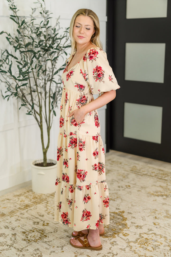 Side view of a woman in the cream red floral puff-sleeve tiered midi dress with tan buckle sandals.

