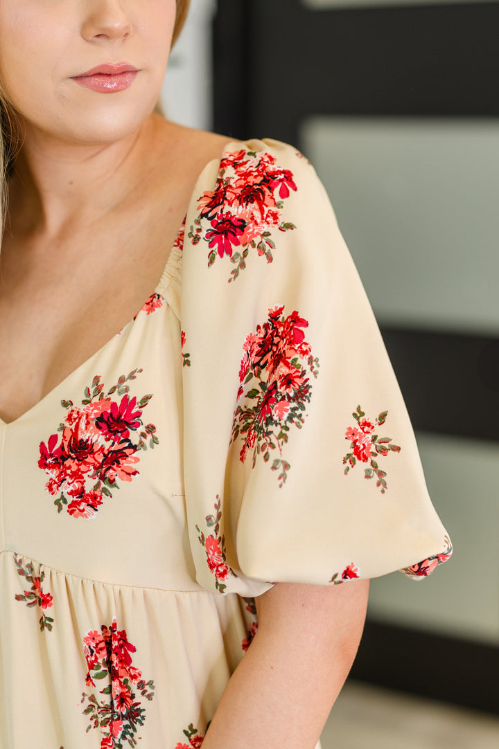 Close-up of the puff sleeve and V-neckline on the cream floral dress with red rose bouquet print.