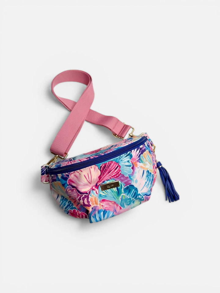 Makeup Junkie Bags colorful seashell print belt bag with pink adjustable strap, navy zipper, and navy tassel on white background