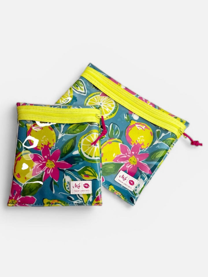 Makeup Junkie Bags set of two clear zip pouches in teal lemon and floral print with yellow zippers and pink zipper pulls on light gray background