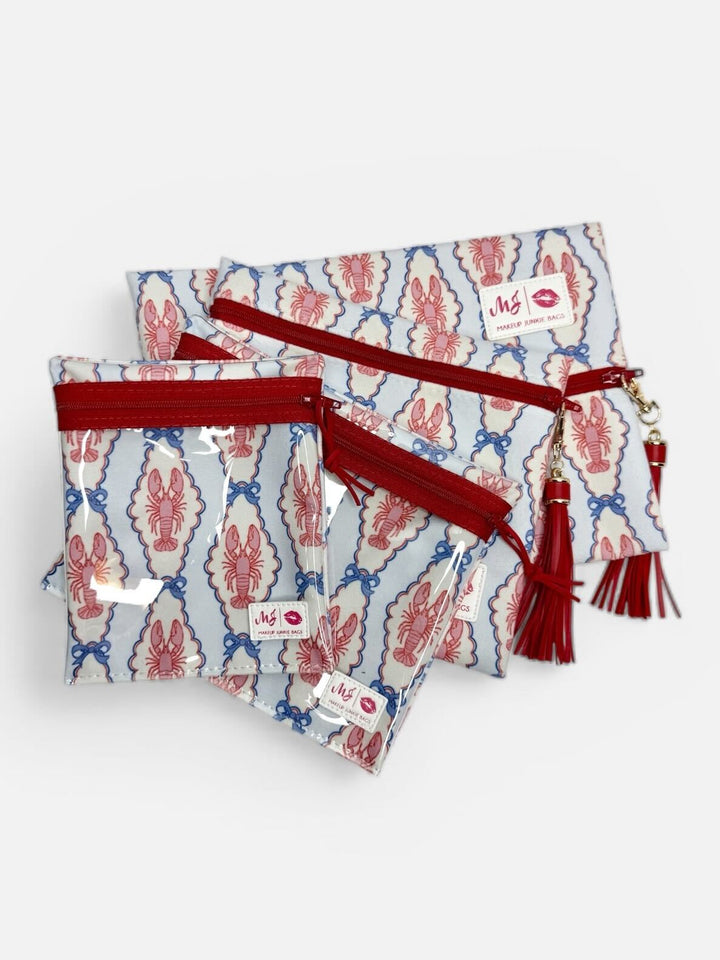 Makeup Junkie Bags set of four zip pouches in pink and blue lobster print with red zippers and red tassels on white background