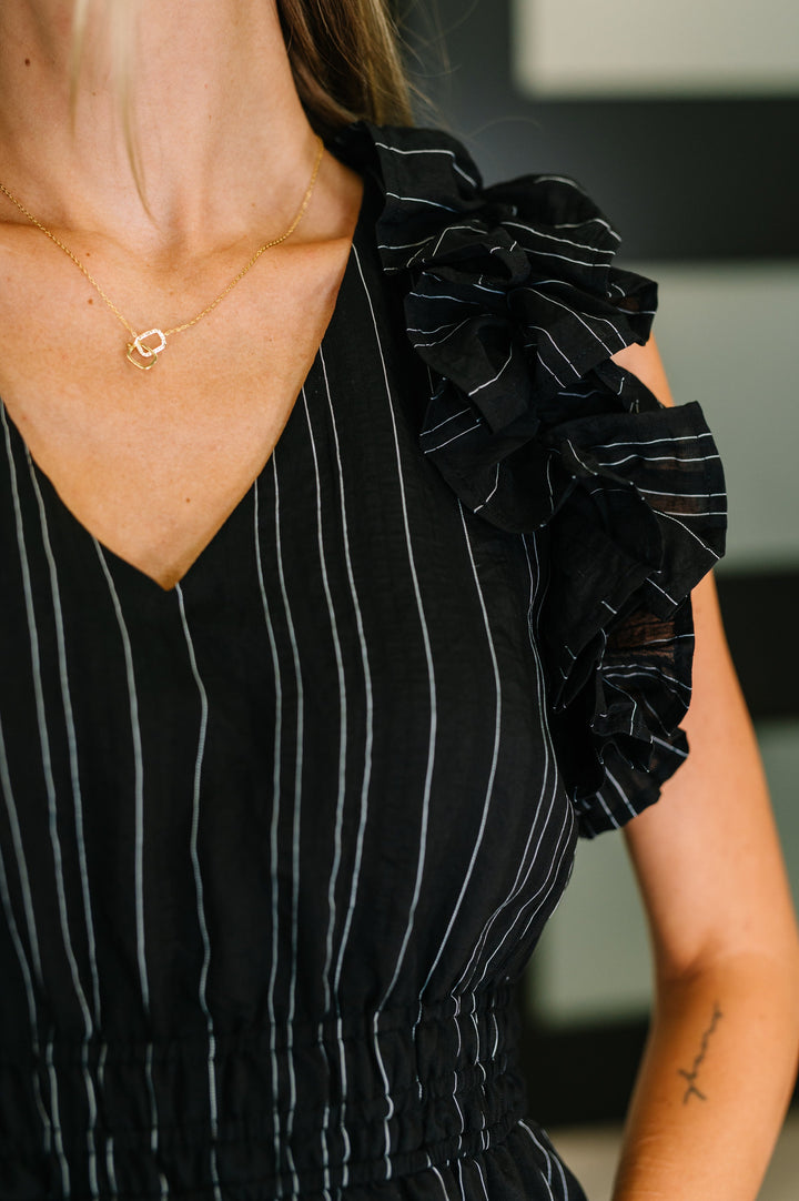 Close-up of black metallic stripe midi dress showing V-neckline, silver pinstripe detail, and ruffle flutter sleeve construction.