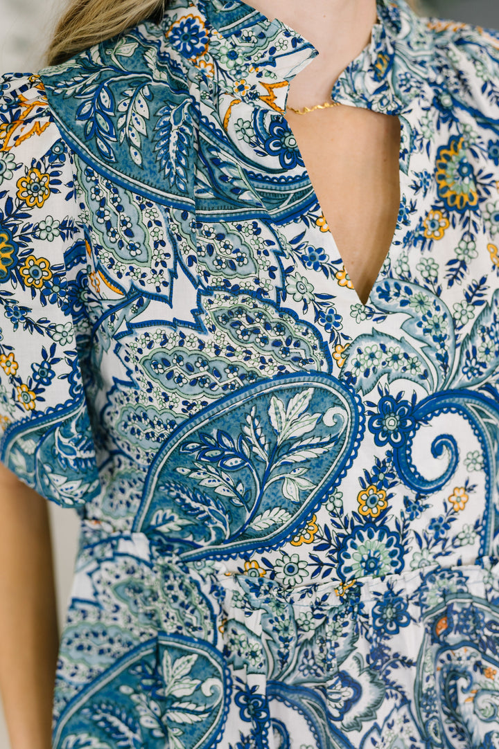 Close-up of the blue and white paisley print V-neckline with ruffle collar detail and gold necklace