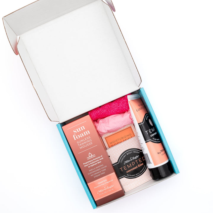 Mixologie Sun Foam Success Kit open teal gift box showing Sun Foam box, Tempted Coconut Kiss Luxury Body Wash, Moisturizing Body Mist, Top Shelf Luxury Lotion, and hot pink tanning application mitt on white background