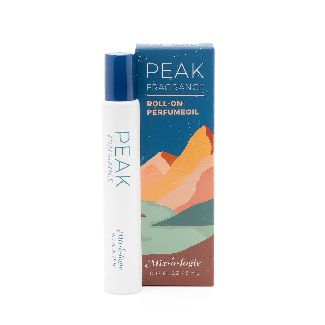 Mixologie Roll-On Perfume Oil in Peak, 5 mL, white rollerball tube with navy cap and teal Peak Fragrance label next to navy starry sky and colorful layered mountain landscape box on white background