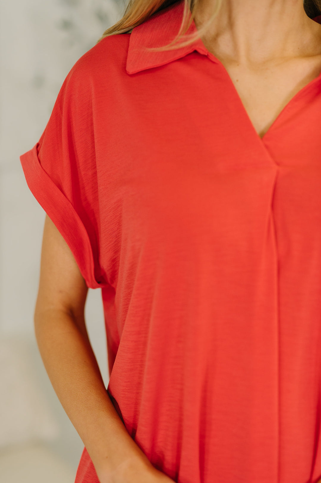 Close-up of coral red short-sleeve collared polo top showing V-neckline, collar detail, and cuffed sleeve.
