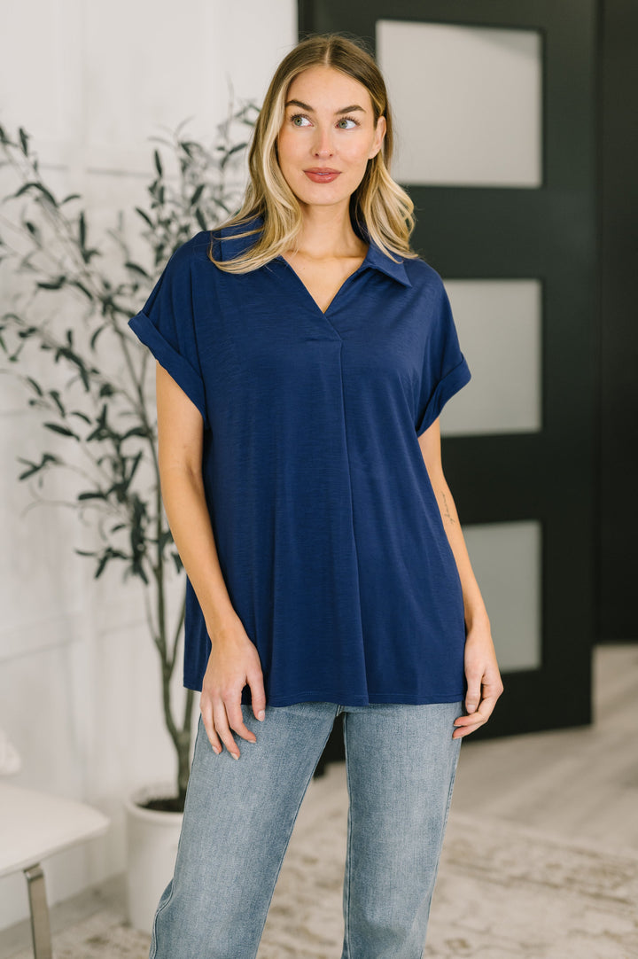 Woman wearing a navy short-sleeve collared polo top with V-neckline and relaxed fit, styled with printed leggings.
