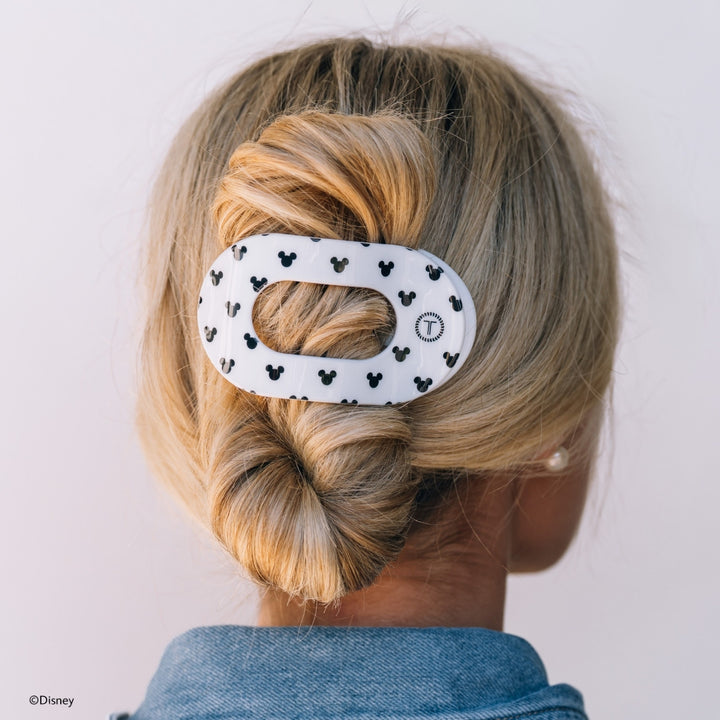Disney x Teleties Mickey Mouse large flat round hair clip in white with allover black Mickey silhouette print securing a twisted low chignon on blonde hair against white background