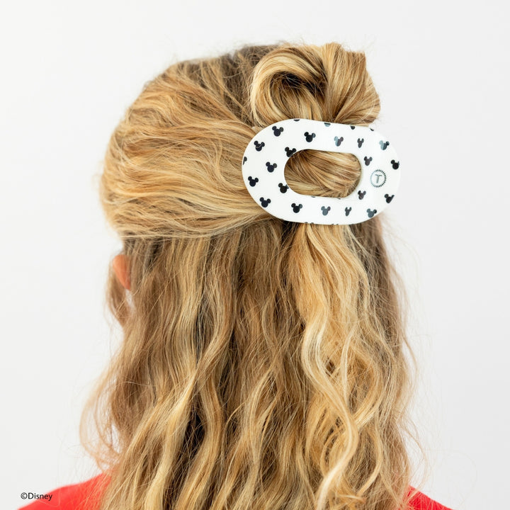 Disney x Teleties Mickey Mouse medium flat round hair clip in white with allover black Mickey silhouette print securing a half-up twisted bun on blonde wavy hair against white background