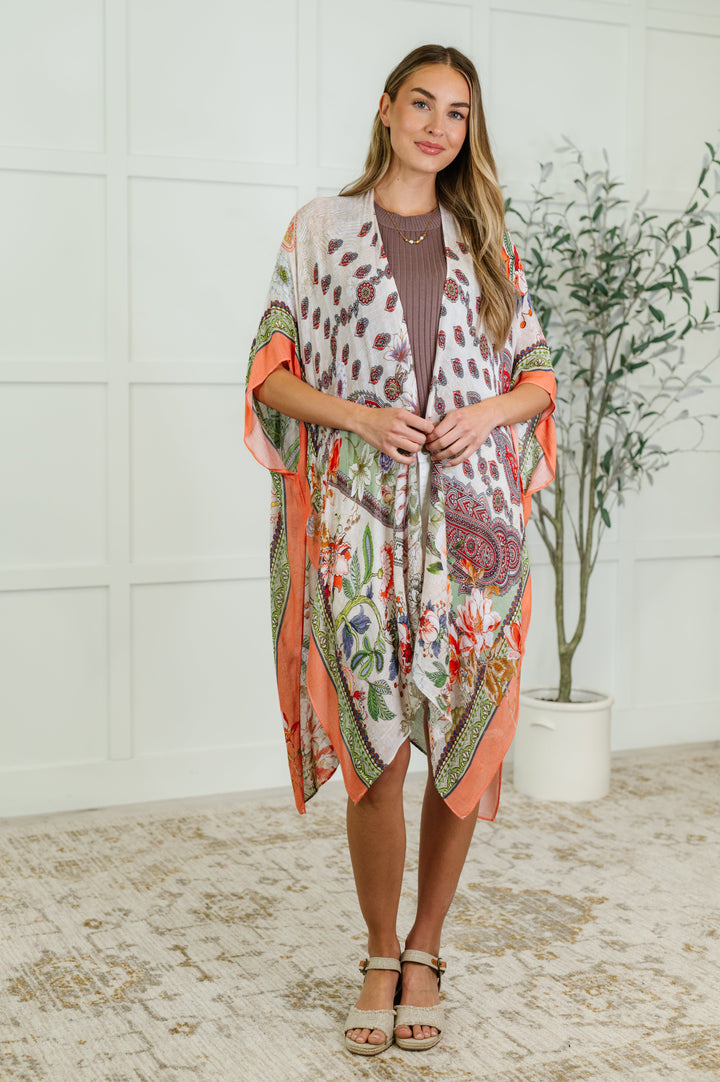 Woman wearing a floral and paisley print kimono with coral trim over a mauve top, paired with gold sandals, full-length view