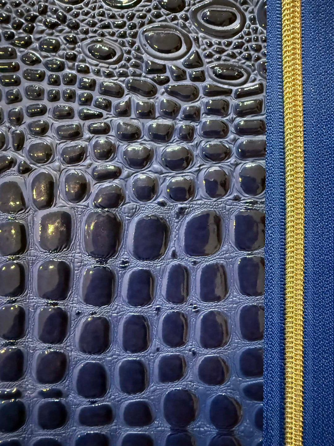 Close-up of blue croc-embossed patent leather with gold zipper detail