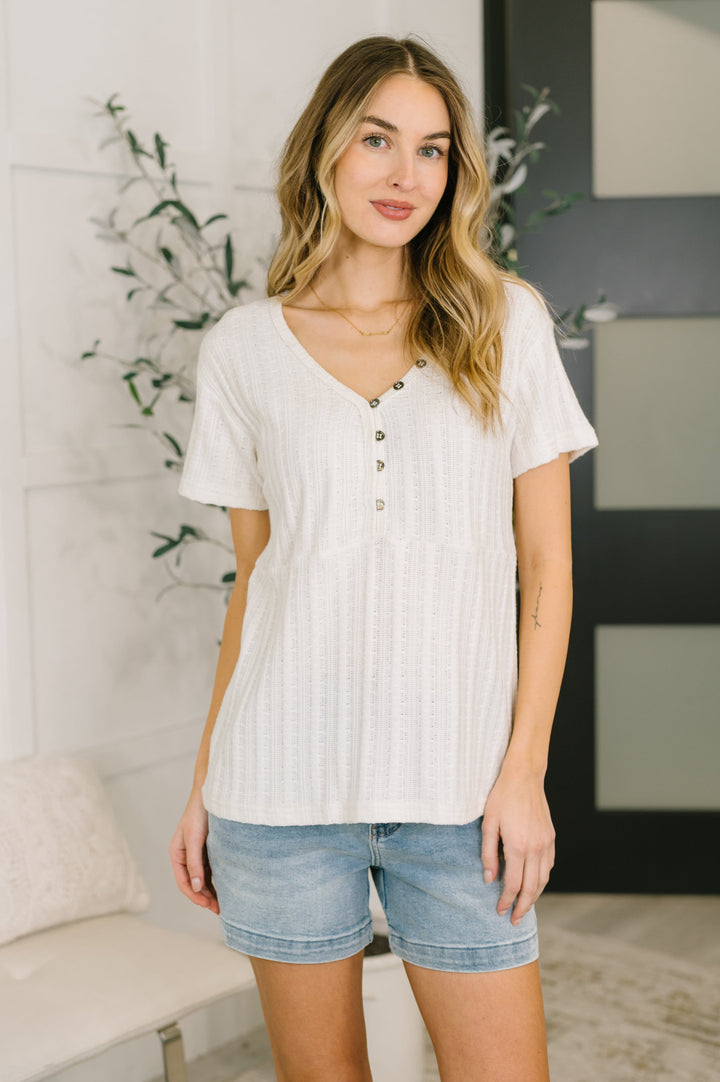 Woman wearing a cream short-sleeve henley top paired with denim shorts