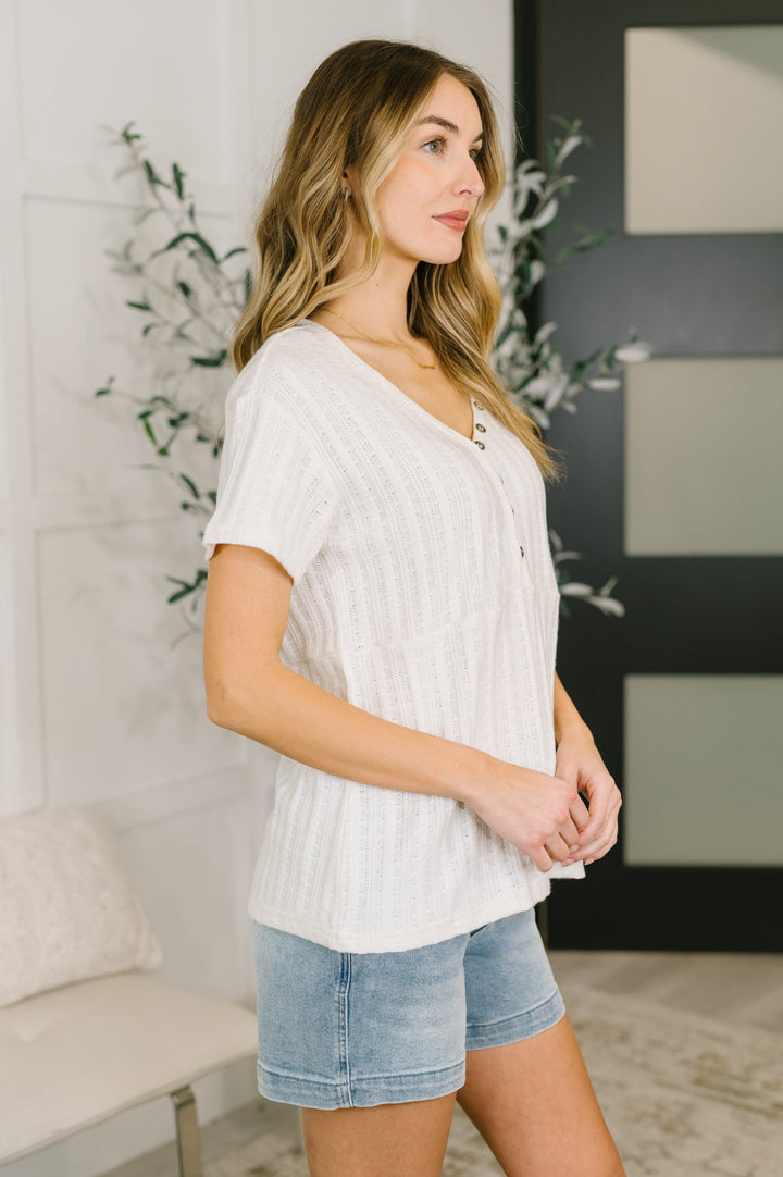 Side view of a woman wearing a cream short-sleeve henley top with denim shorts