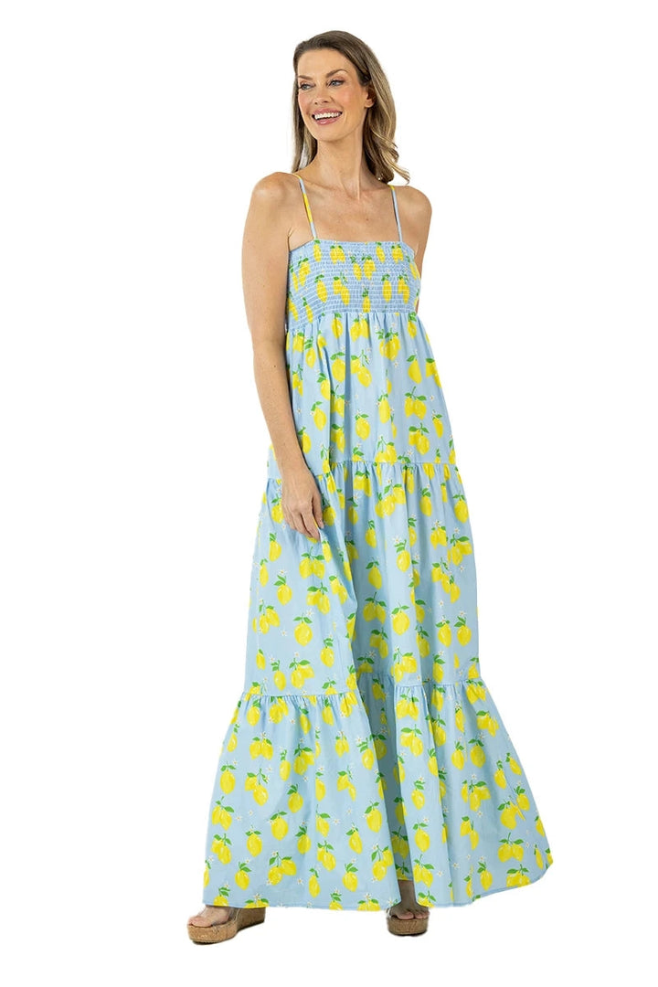 Front view of smiling woman in a light blue lemon print smocked tiered maxi dress with spaghetti straps and wood-heel sandals.