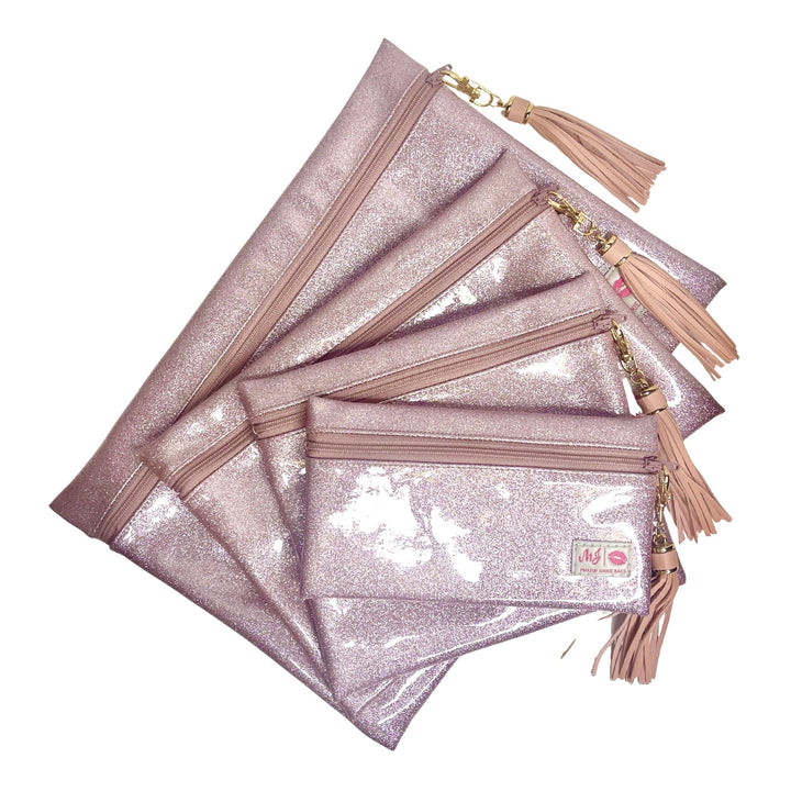 Makeup Junkie Bags blush pink glitter clear vinyl zip bags in four sizes fanned out with blush tassel zipper pulls and branded patches, front view on white background