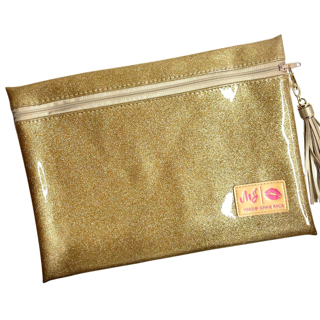 Makeup Junkie Bags gold glitter clear vinyl zip makeup bag with gold tassel zipper pull and branded patch, front view on white background