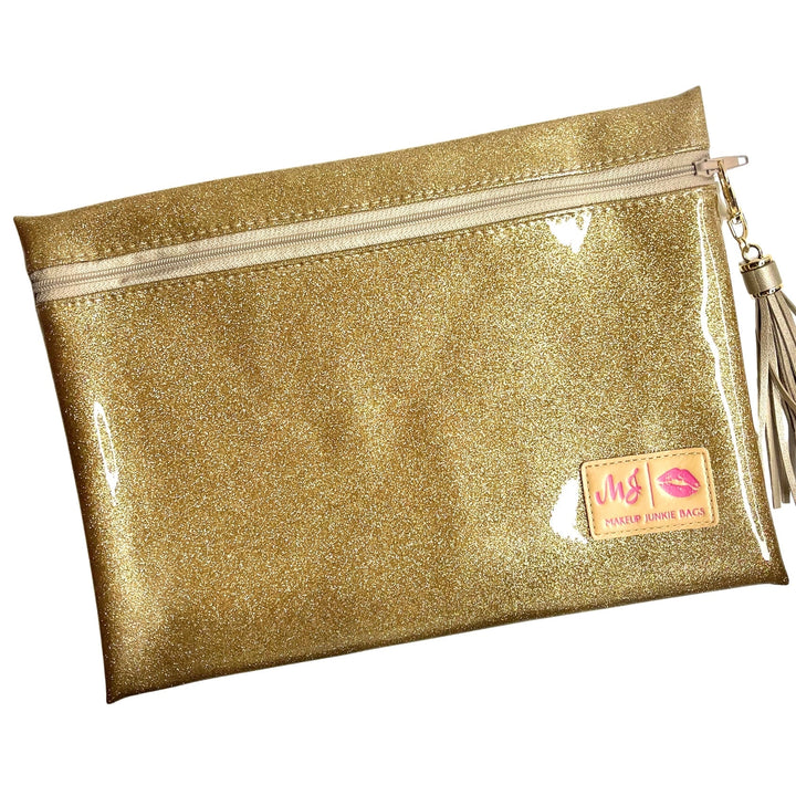 Makeup Junkie Bags gold glitter clear vinyl zip makeup bag with gold tassel zipper pull and branded patch, front view on white background