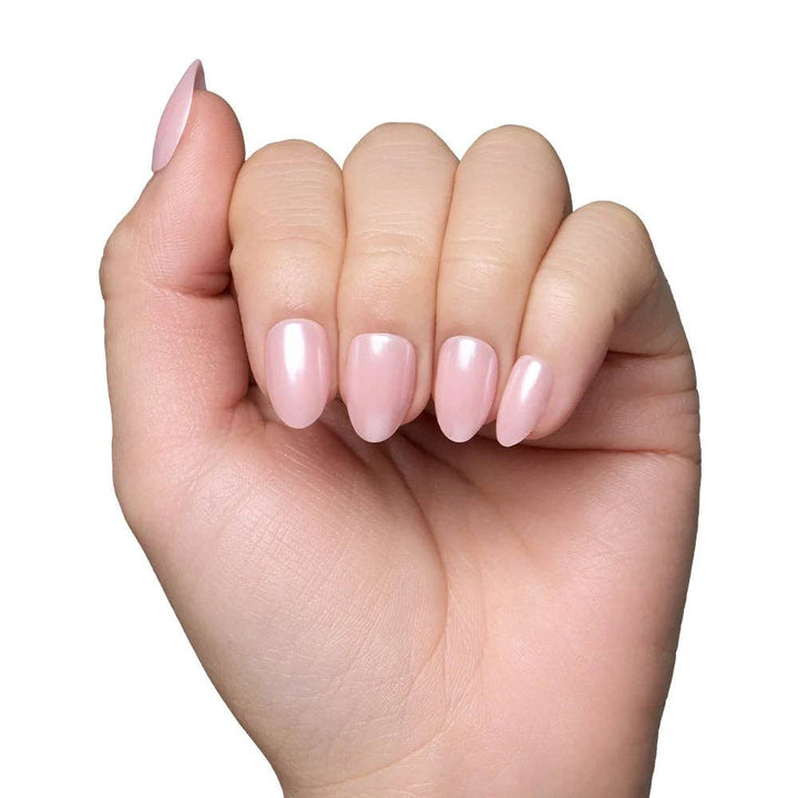Close-up of blush pink short oval press-on nails worn on fair skin tone hand against white background
