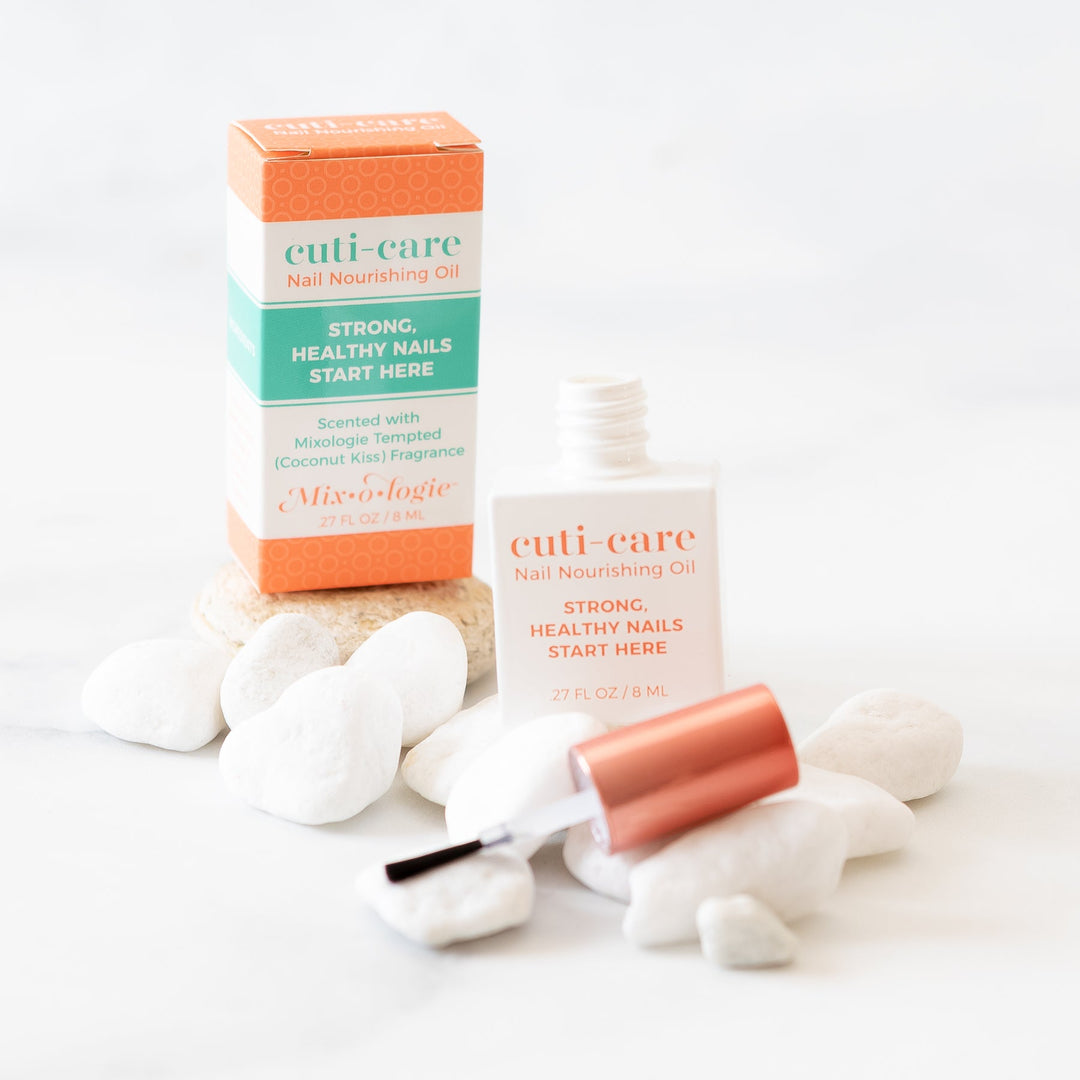 Mixologie Cuti-Care Nail Nourishing Oil, 0.27 fl oz, open bottle with brush applicator displayed next to orange box on white surface with white river rocks