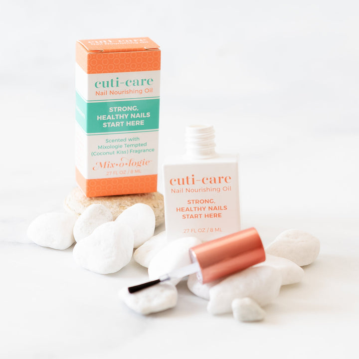 Mixologie Cuti-Care Nail Nourishing Oil, 0.27 fl oz, open bottle with brush applicator displayed next to orange box on white surface with white river rocks