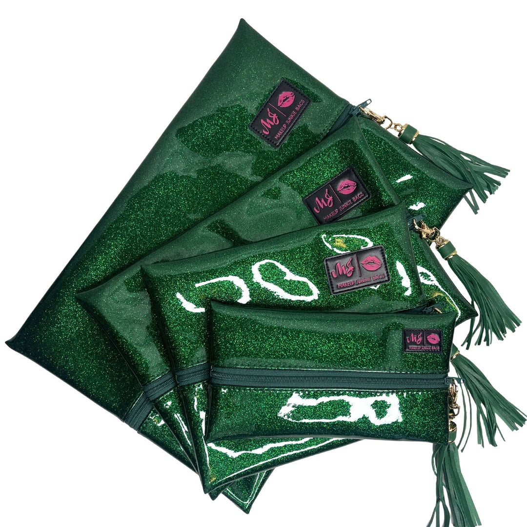 Makeup Junkie Bags emerald green glitter clear vinyl zip bags in four sizes fanned out with green tassel zipper pulls and branded patches, front view on white background