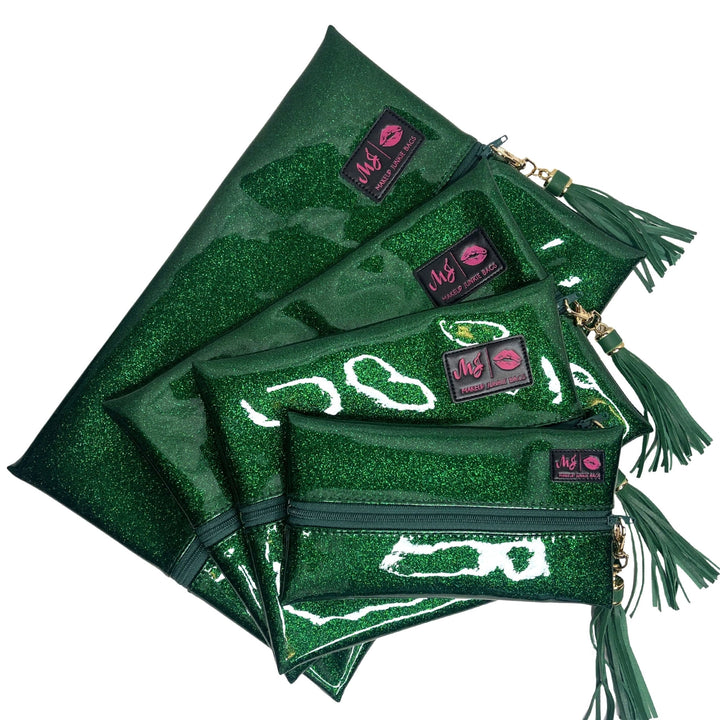Makeup Junkie Bags emerald green glitter clear vinyl zip bags in four sizes fanned out with green tassel zipper pulls and branded patches, front view on white background