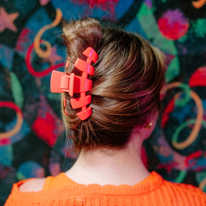 Woman wearing large Teleties coral red claw clip in an updo bun hairstyle