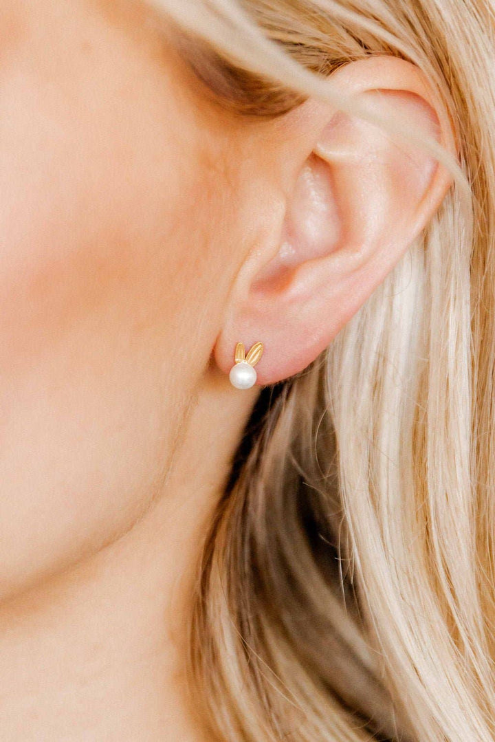 Close-up of gold bunny ear and pearl stud earring worn on ear with blonde hair.