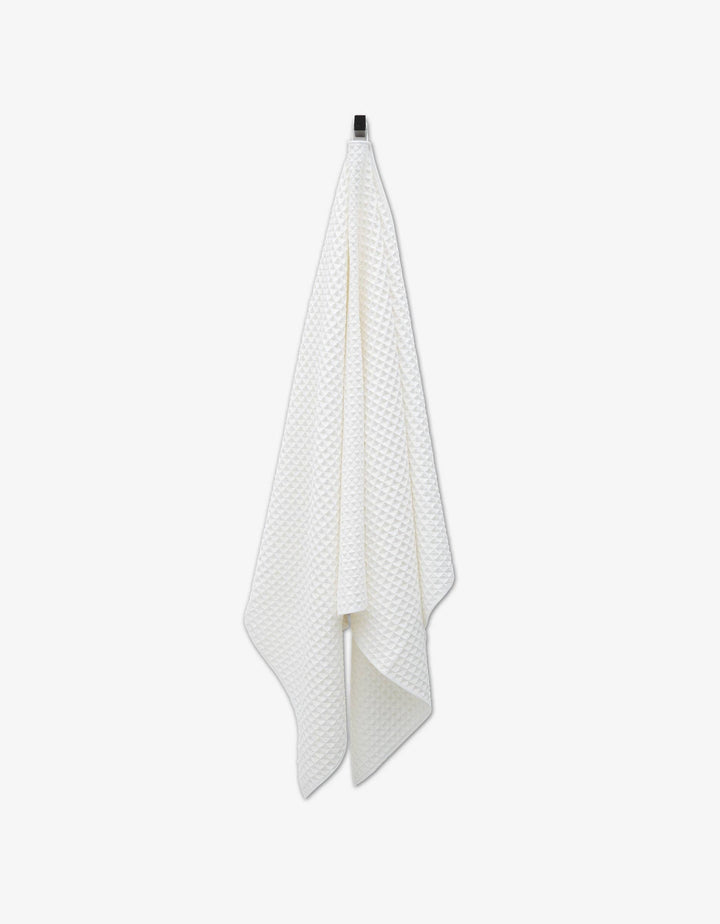 White Cloud Waffle Bath Towel by Geometry hanging on a hook against a white background