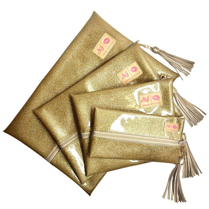 Makeup Junkie Bags gold glitter clear vinyl zip bags in four sizes fanned out with gold tassel zipper pulls, flat lay on white background