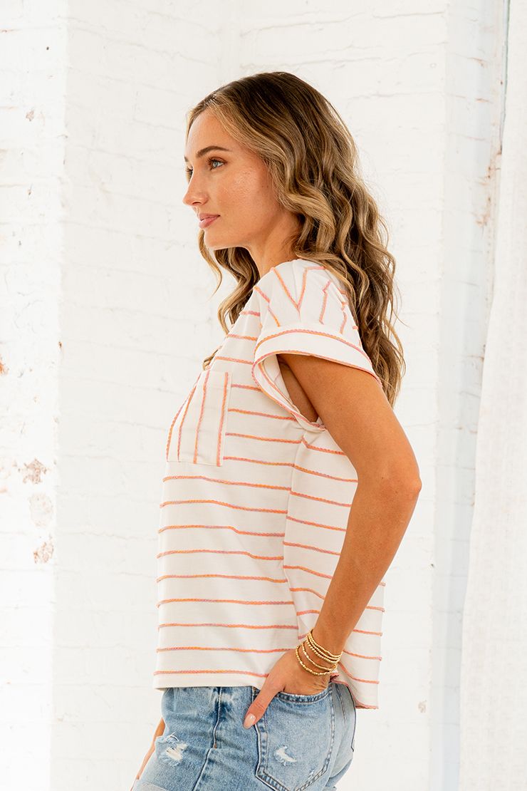 Side view of woman wearing a cream and orange stripe short sleeve top with cuffed sleeves and chest pocket.
