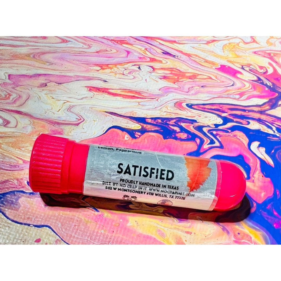 No Crap In It Satisfied essential inhaler with hot pink cap, made with lemon and peppermint, lying on a colorful pink, blue, and yellow swirled paint background.
