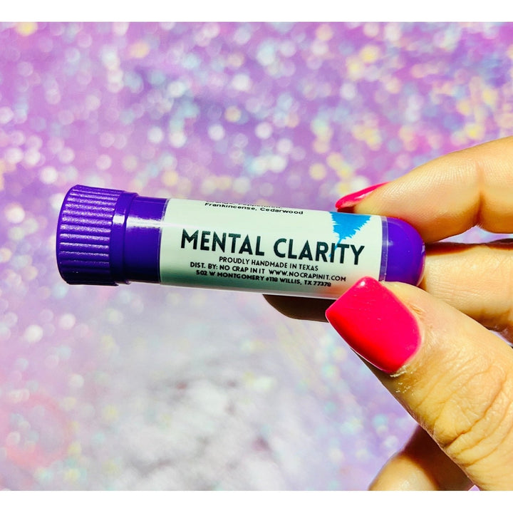 Hand with hot pink nails holding a No Crap In It Mental Clarity essential inhaler with purple cap, made with frankincense and cedarwood, against a sparkly pink and purple glitter background.