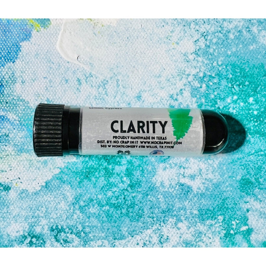 No Crap In It Clarity essential inhaler with black cap, made with lemon and cypress, lying on a blue and white paint splatter background.