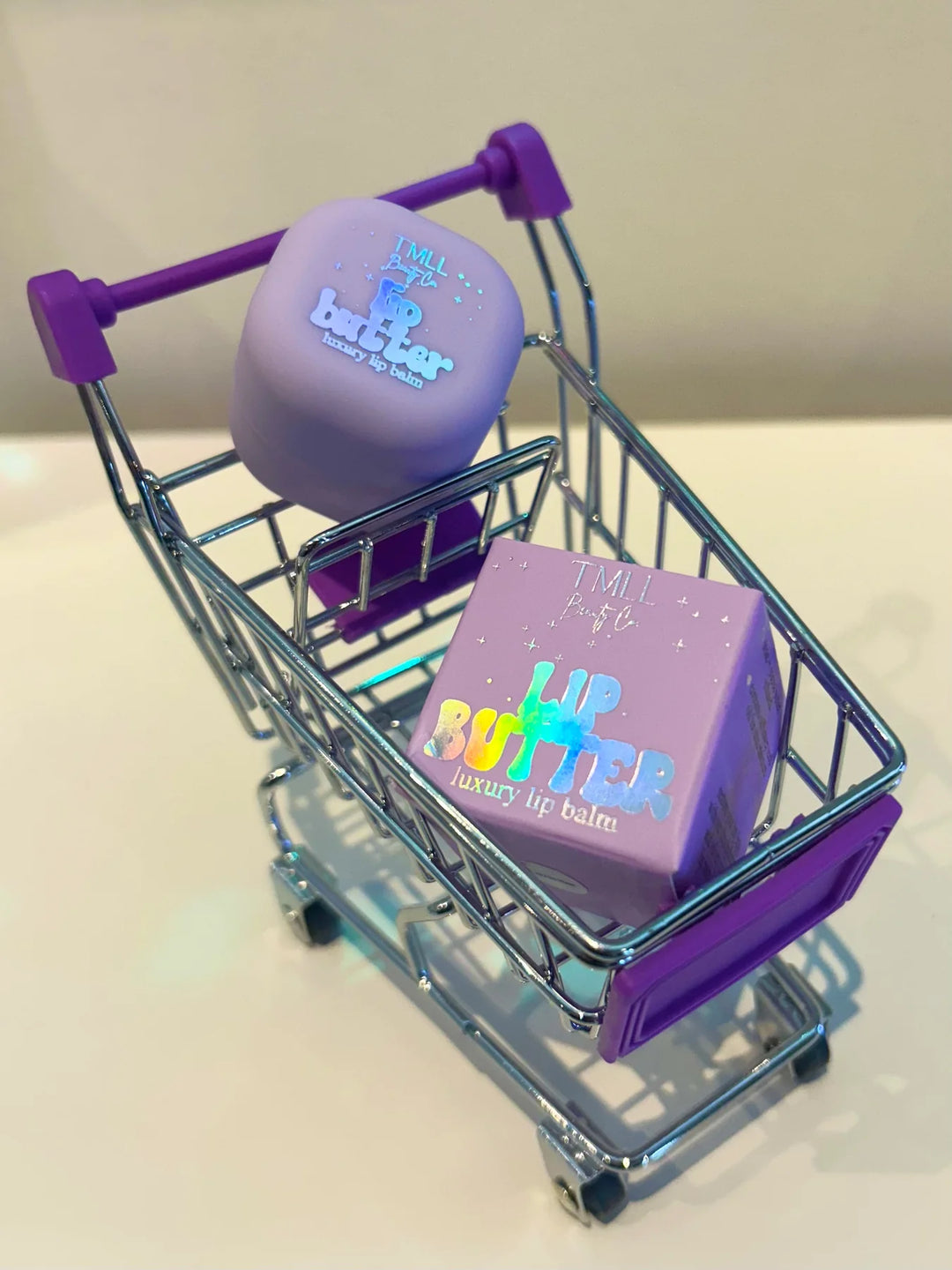 TMLL Purple Lip Butter luxury lip balm ball and square compact displayed in a miniature silver shopping cart