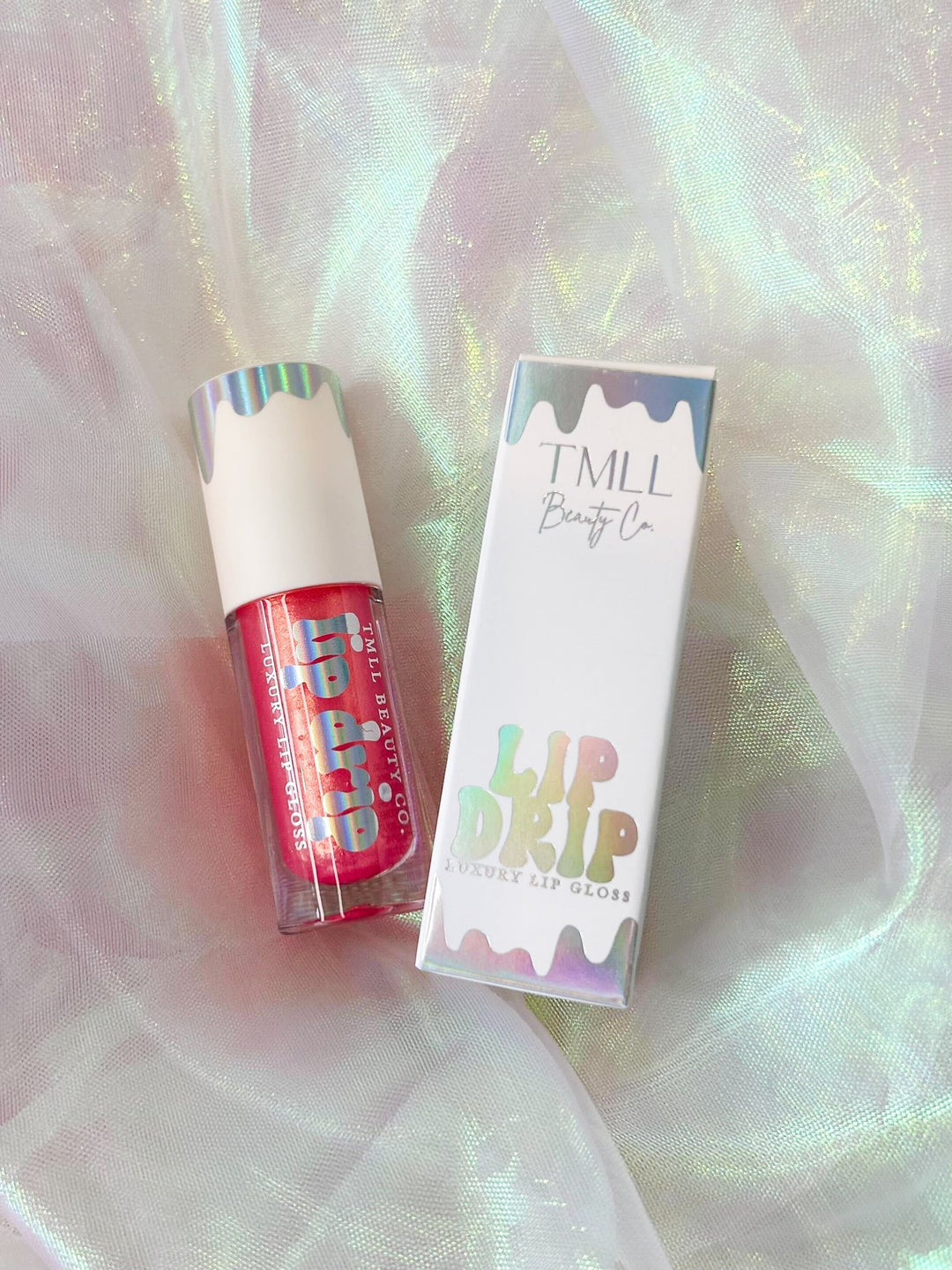 TMLL Beauty Co. Lip Drip Luxury Lip Gloss in a red shade with holographic tube and gift box on an iridescent fabric background