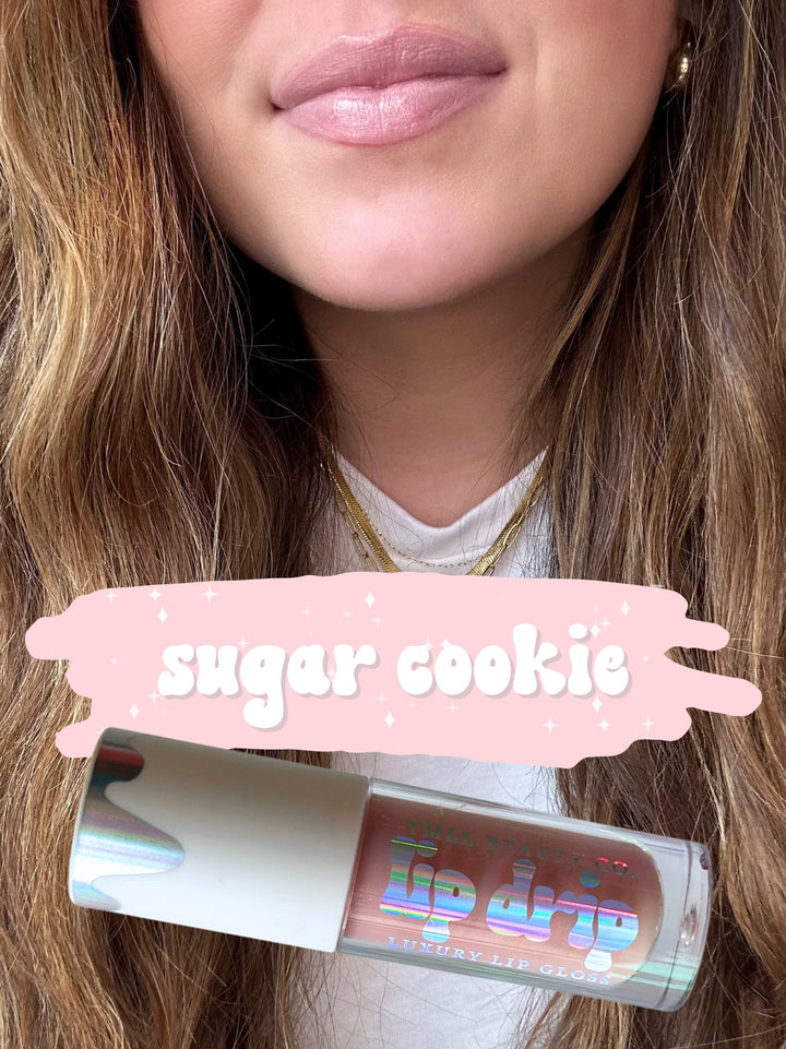 TMLL Beauty Co. Lip Drip Luxury Lip Gloss in Sugar Cookie — a sheer nude-pink shade shown on lips with holographic tube below