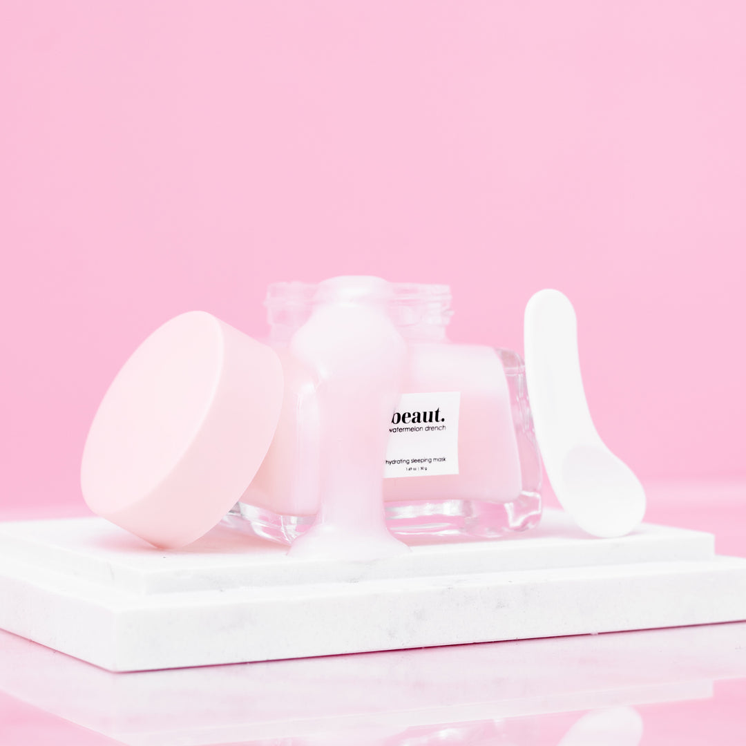 Beaut Watermelon Drench Hydrating Sleeping Mask 50g open glass jar with lid and spatula on white marble tray against pink background