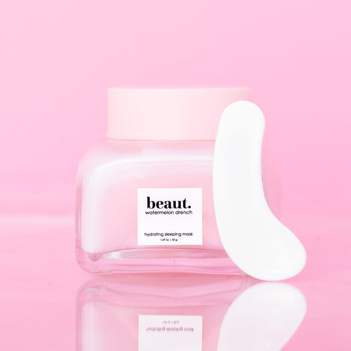 Beaut Watermelon Drench Hydrating Sleeping Mask 50g closed glass jar with pink lid and white spatula leaning against jar on pink reflective surface