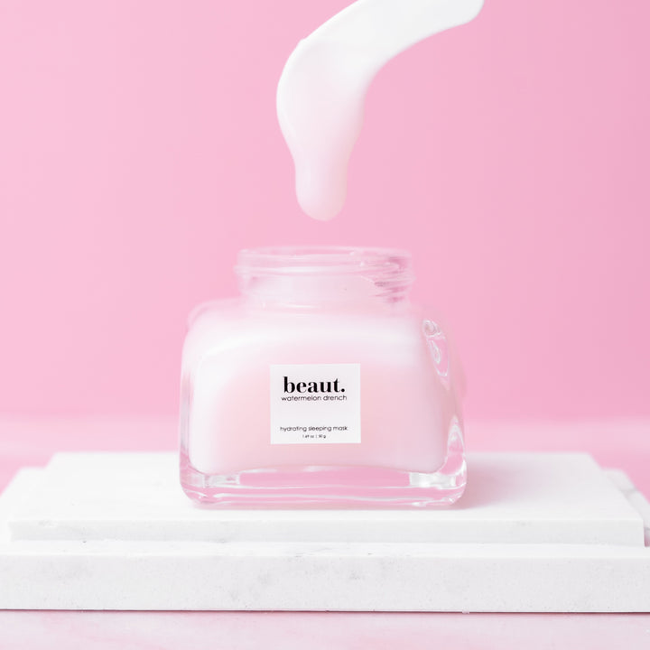 Beaut Watermelon Drench Hydrating Sleeping Mask 50g open glass jar with white cream being poured in on pink background