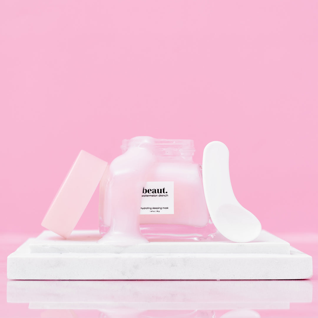 Beaut Watermelon Drench Hydrating Sleeping Mask 50g open glass jar with lid and spatula displayed on white marble tray against pink background